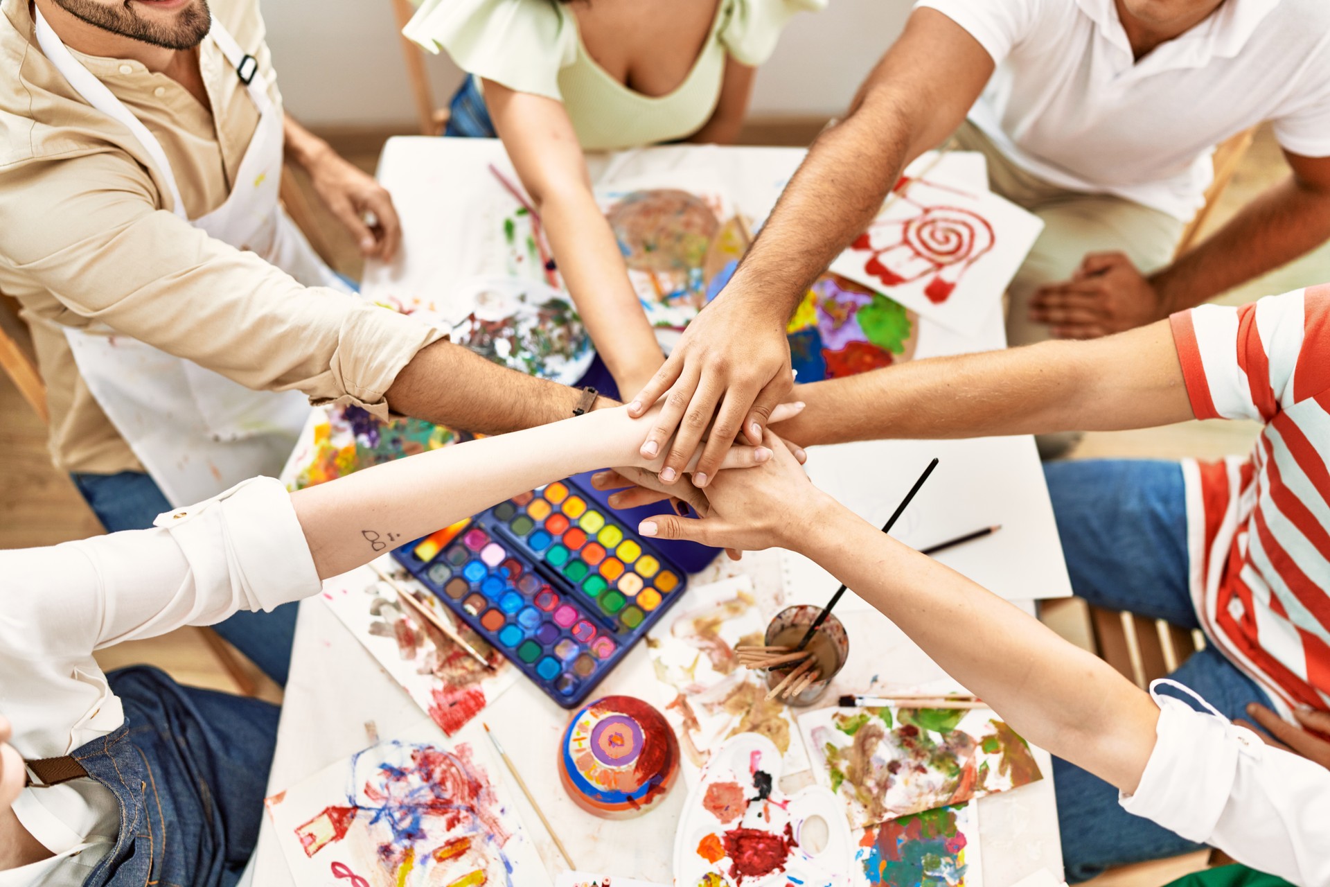 Group of people sitting on the table with united hands at art studio.