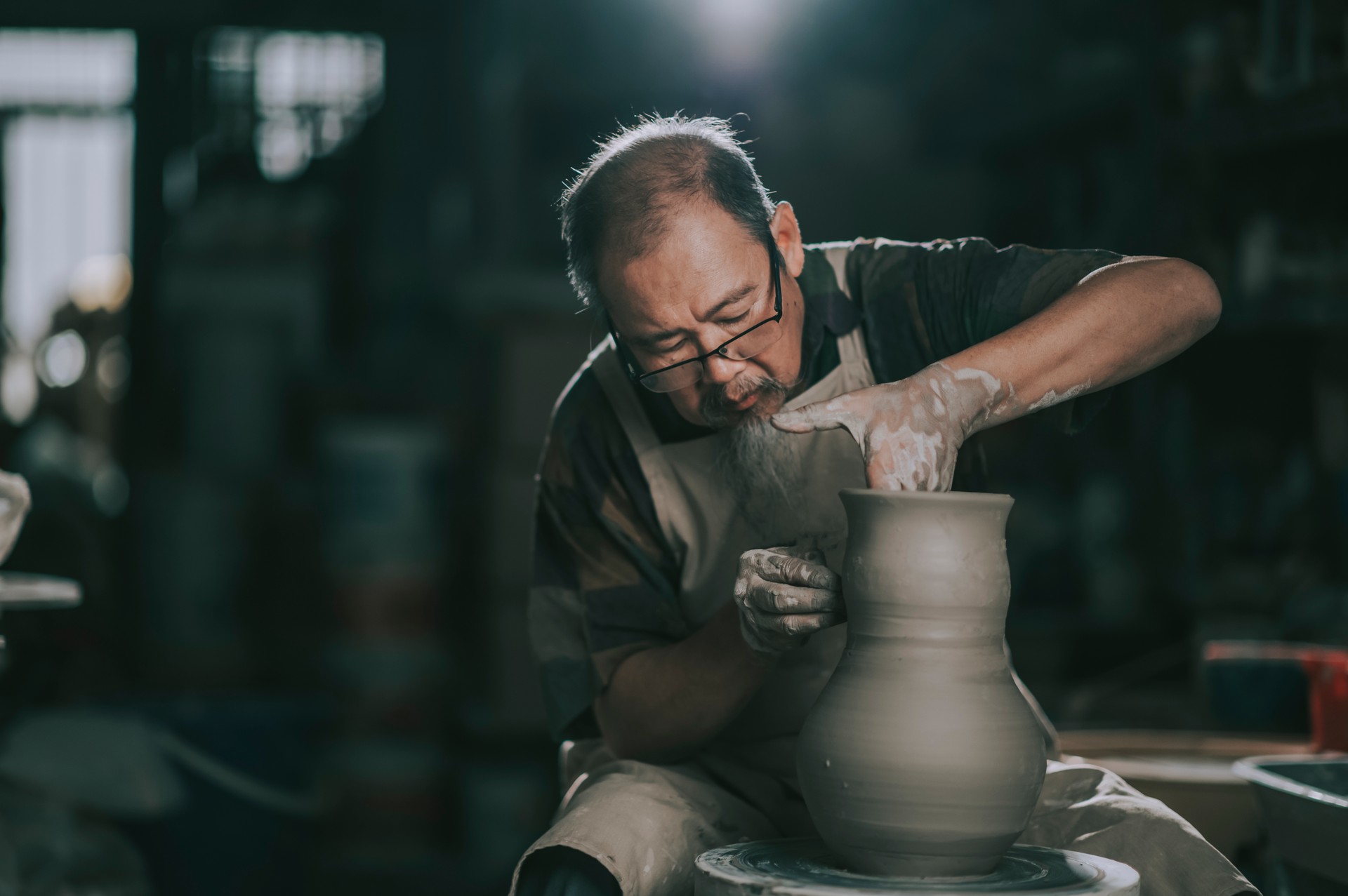 asian chinese senior man clay artist working in his studio with spinning pottery wheel