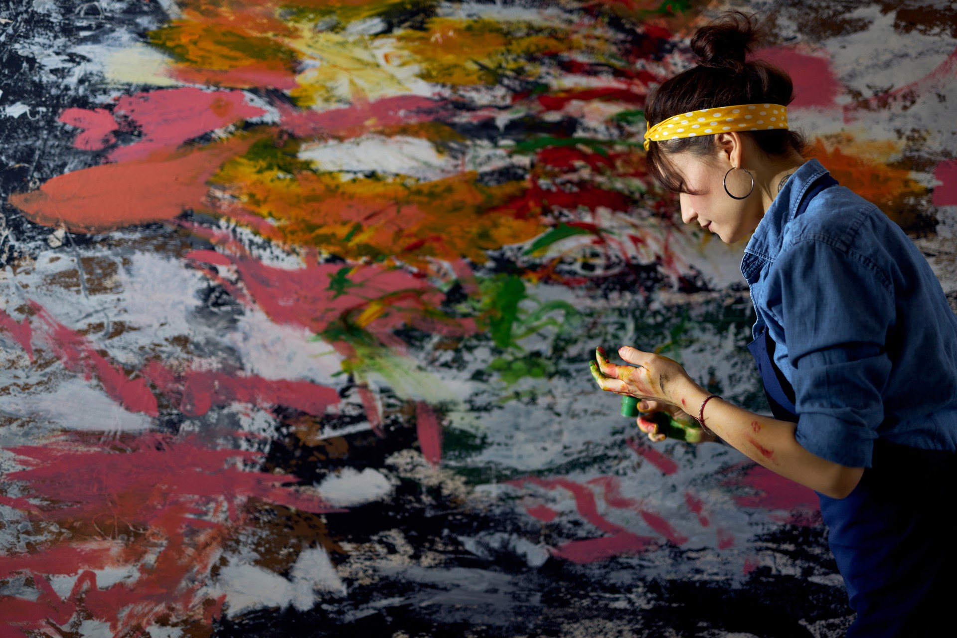 Side view of young female painter creating a large modern abstract oil painting, applying paint on canvas with fingers in workshop